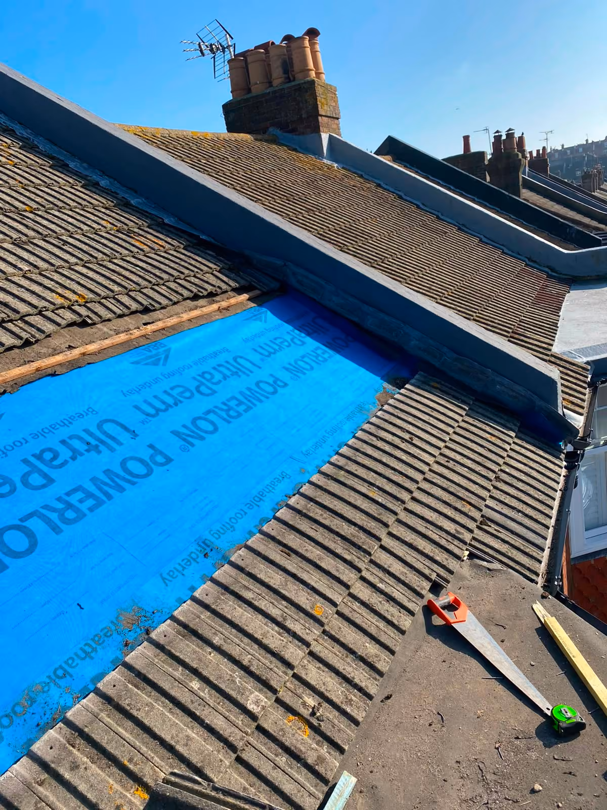 Blue breathable underlay dressed across a pitched roof beside the old tiles